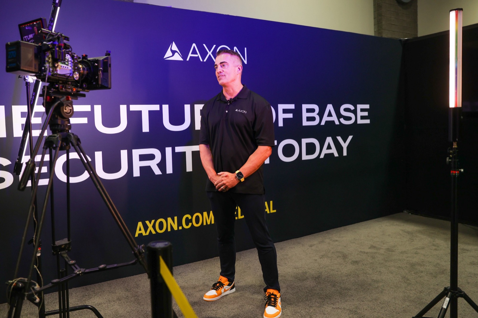 A cinema camera filming an Axon executive in front of a wall reading The future of base security today