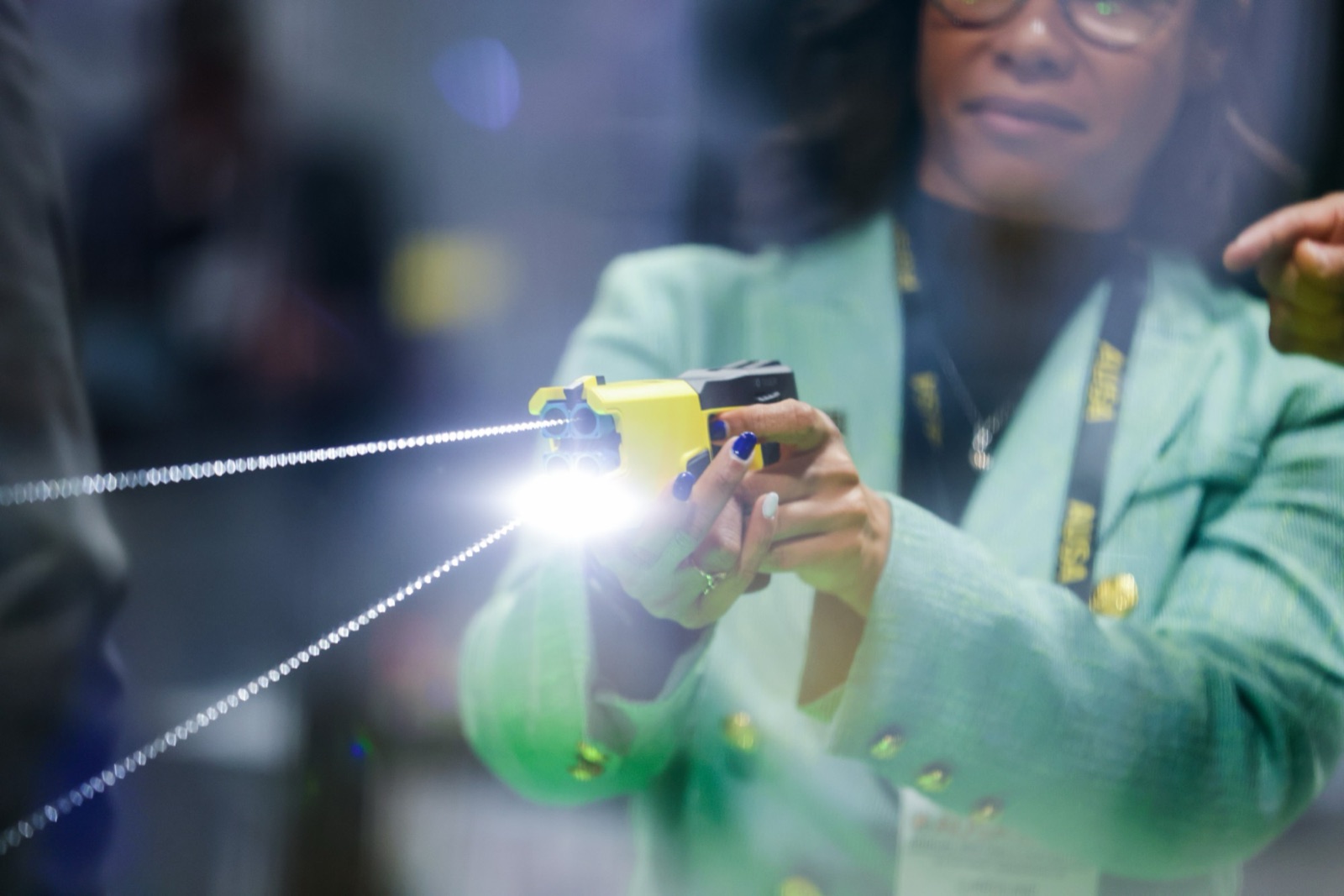 An attendee firing a TASER 10 in the demo range, the probes catching the light