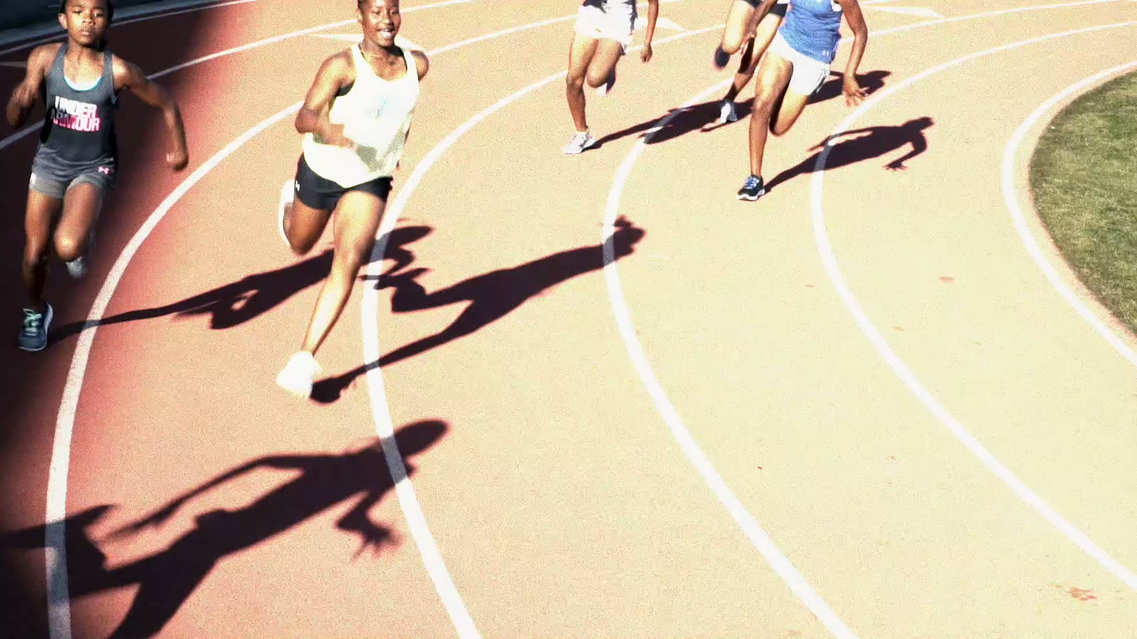 Girls sprinting on a track, long shadows behind them